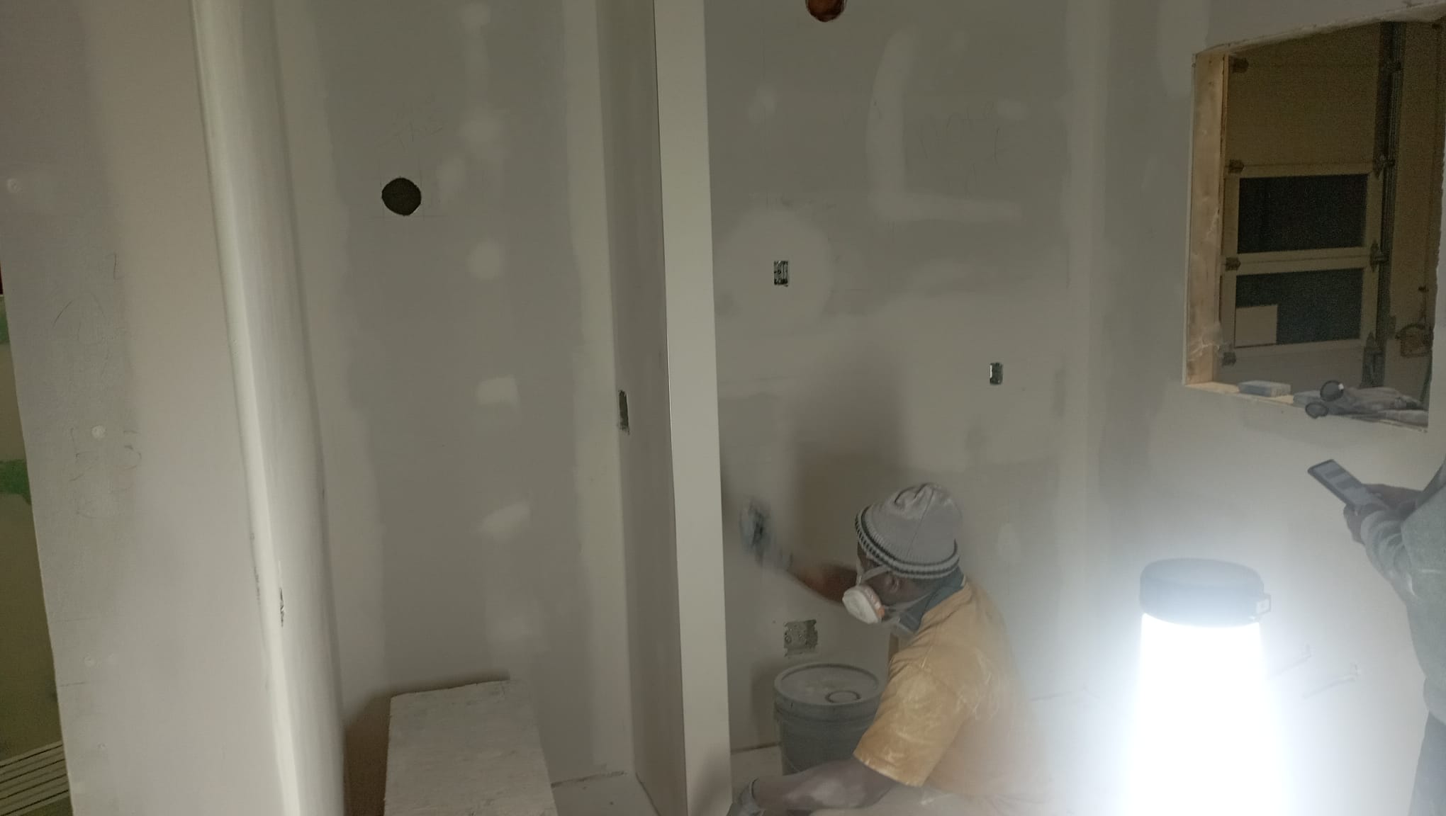Crew sanding mudded drywall on site with respirator and work light