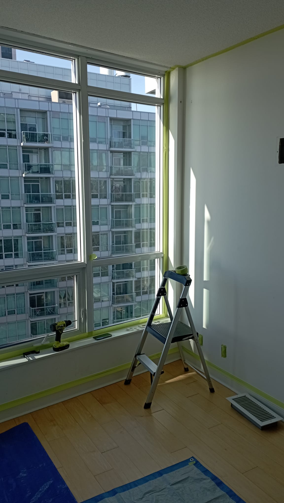 High-rise condo bedroom prepped with green painter's tape on tall windows and baseboards