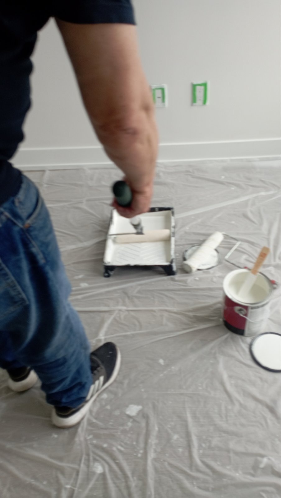Owner loading paint onto roller on covered floor