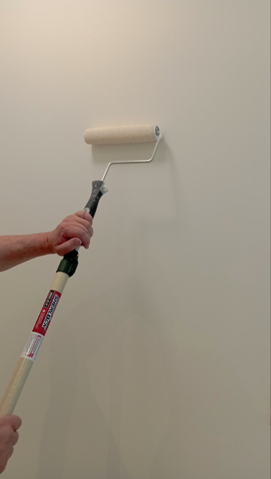 Painter rolling fresh paint onto a wall with an extension pole