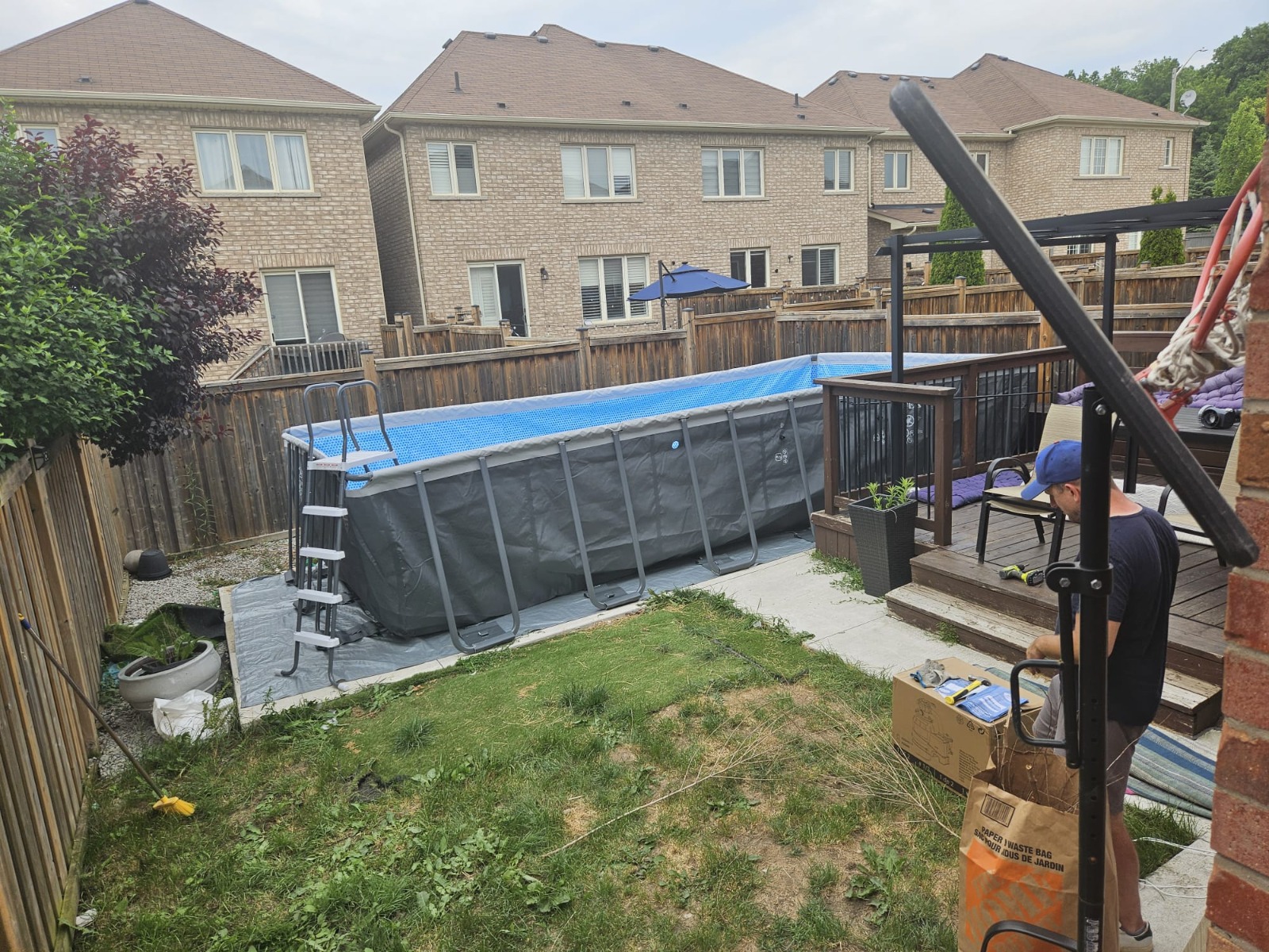 Above-ground pool installed with a fresh wood deck and patio chairs in a backyard